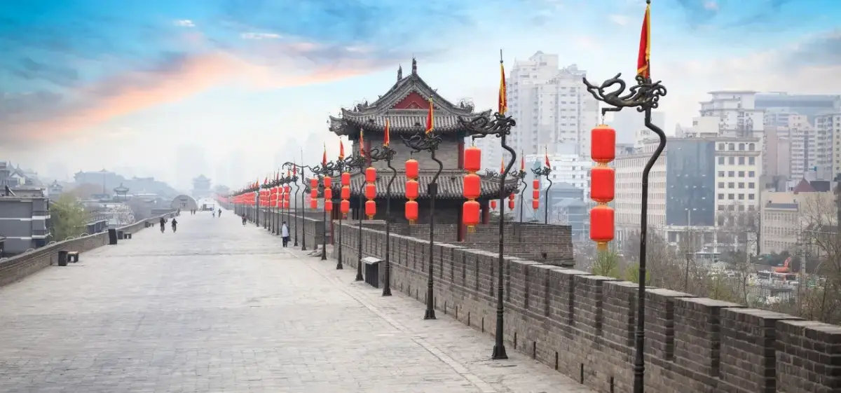 Ancient Xi'an city wall adorned with traditional red lanterns overlooking modern skyline at sunset