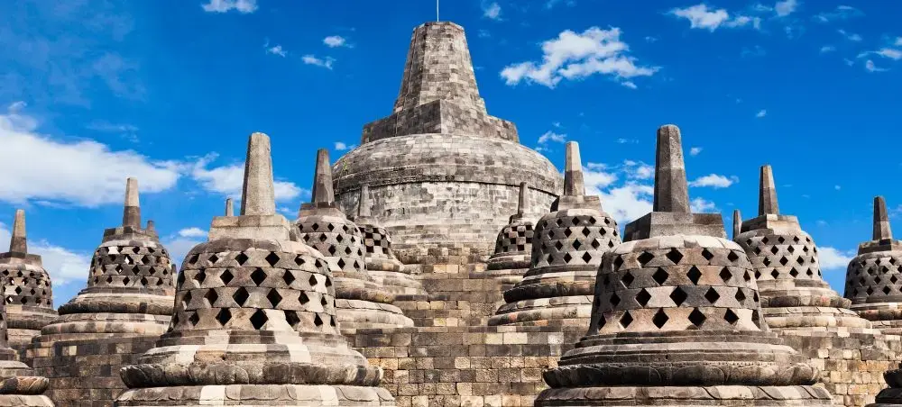 Ancient Borobudur temple with intricate stone stupas and central dome under blue sky in Yogyakarta, Indonesia