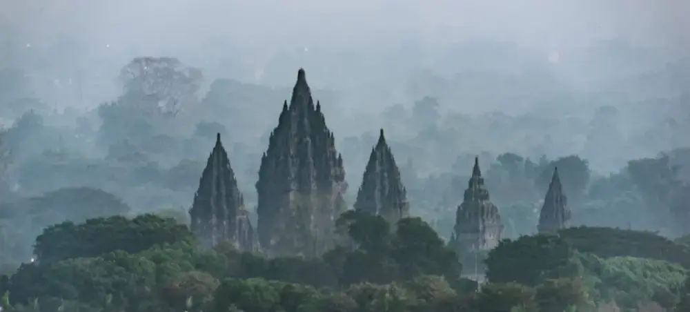 Ancient Prambanan temple complex rising through misty tropical forest near Yogyakarta, Indonesia