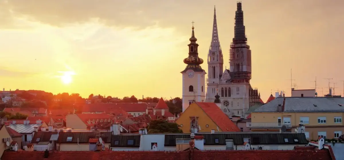 Zagreb Cathedral towers rise majestically above red-tiled rooftops during golden sunset over Croatia's capital city