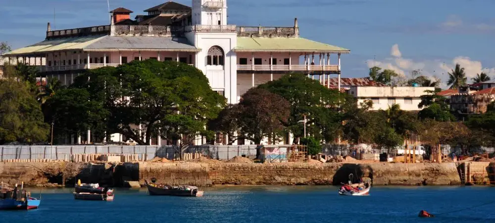 Historic Stone Town waterfront in Zanzibar with traditional dhow boats anchored in turquoise harbor waters