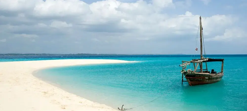 Traditional dhow sailing boat anchored in crystal-clear turquoise waters off pristine Zanzibar beach