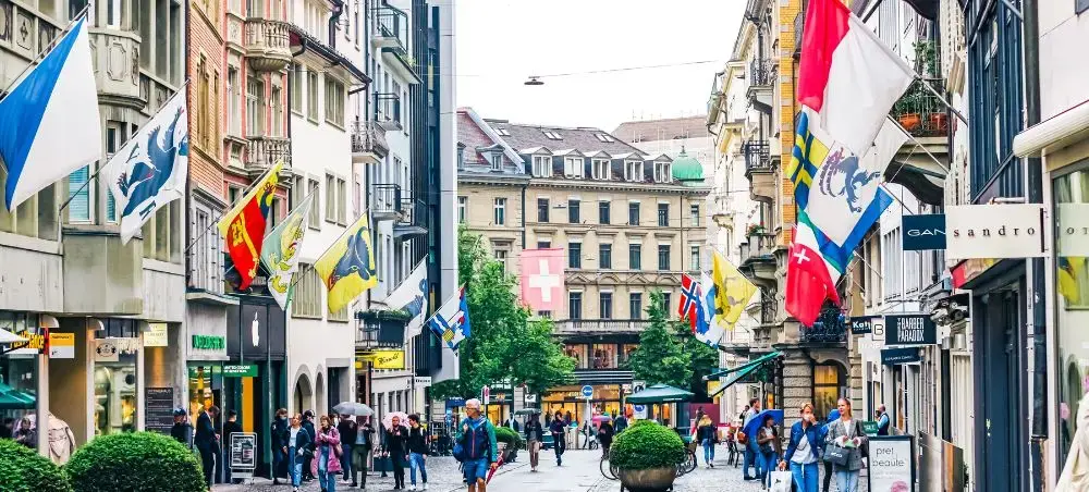 Bustling pedestrian street in Zurich's historic center with colorful flags and traditional Swiss architecture