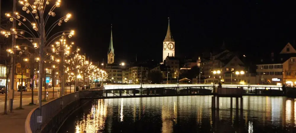 Zurich's illuminated historic center at night with church spires reflecting in the Limmat River