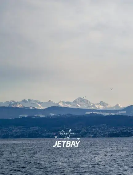 Snow-capped Swiss Alps rising majestically above Lake Zurich with Jetbay branding for luxury travel