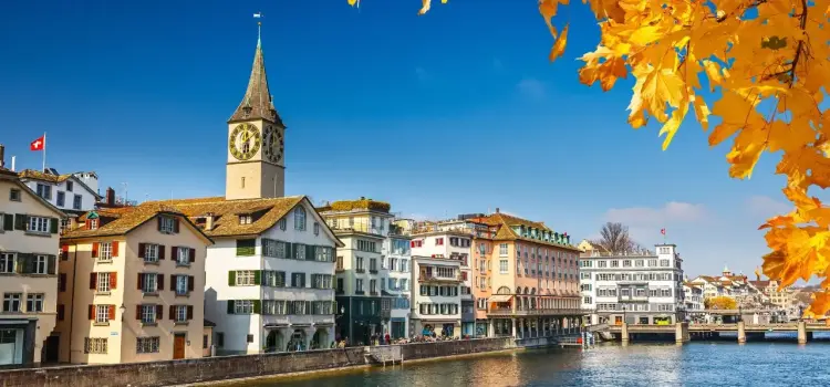 Historic Zurich waterfront with colorful medieval buildings and iconic clock tower in autumn sunlight