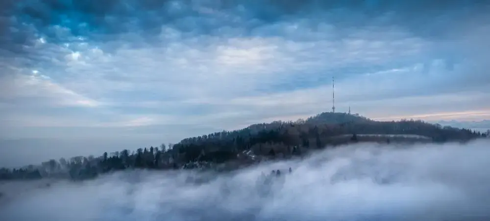 Misty clouds enveloping forested hills with communication tower near Zurich, showcasing Switzerland's scenic landscapes