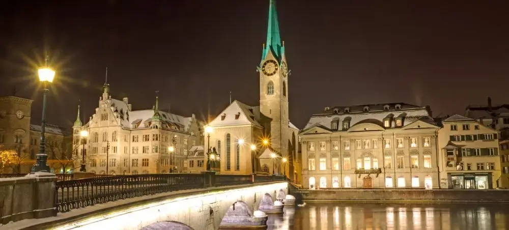 Historic Zurich waterfront at night featuring illuminated Fraumünster church and traditional Swiss architecture