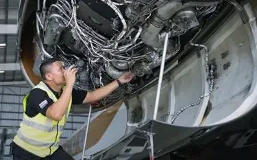 Aircraft maintenance technician inspecting complex wiring systems inside private jet engine compartment