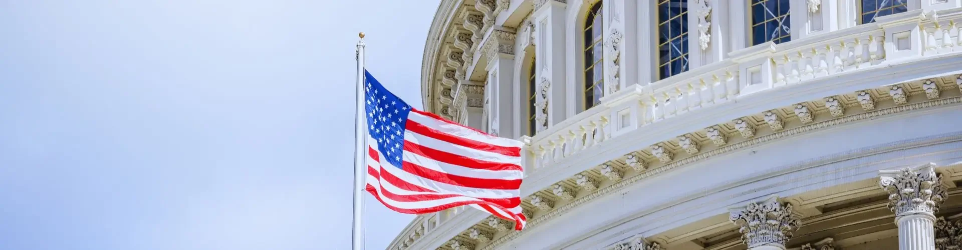 American flag waving beside the iconic white dome and columns of the US Capitol building in Washington DC