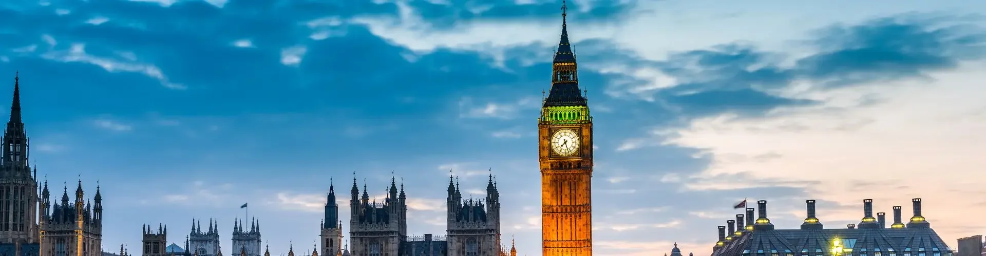 Westminster Palace and Big Ben illuminated at dusk beside Thames River for UK private jet travel guide
