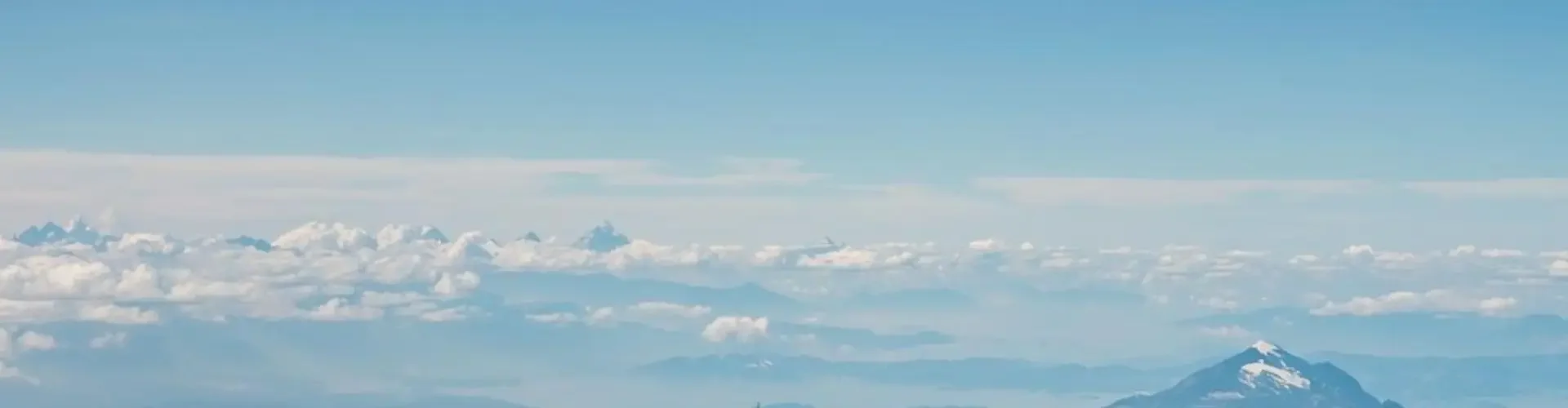 White private jet soaring above snow-capped Canadian mountain ranges under cloudy blue skies