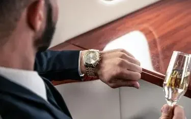 What Is the Least Expensive Way to Fly Privately? Business executive checking luxury watch while holding champagne glass aboard private jet cabin