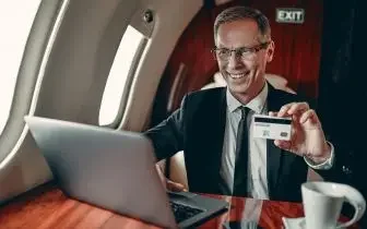 Business executive enjoying luxury private jet travel while working on laptop and holding membership card