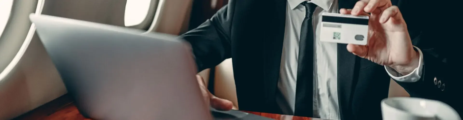 How Much Does a Private Jet Membership Cost? Smiling businessman using laptop and holding credit card aboard luxury private jet cabin