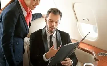 Business executive reviewing documents while flight attendant provides personalized service aboard luxury jet