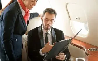 Business executive reviewing documents on tablet while flight attendant provides service aboard luxury aircraft