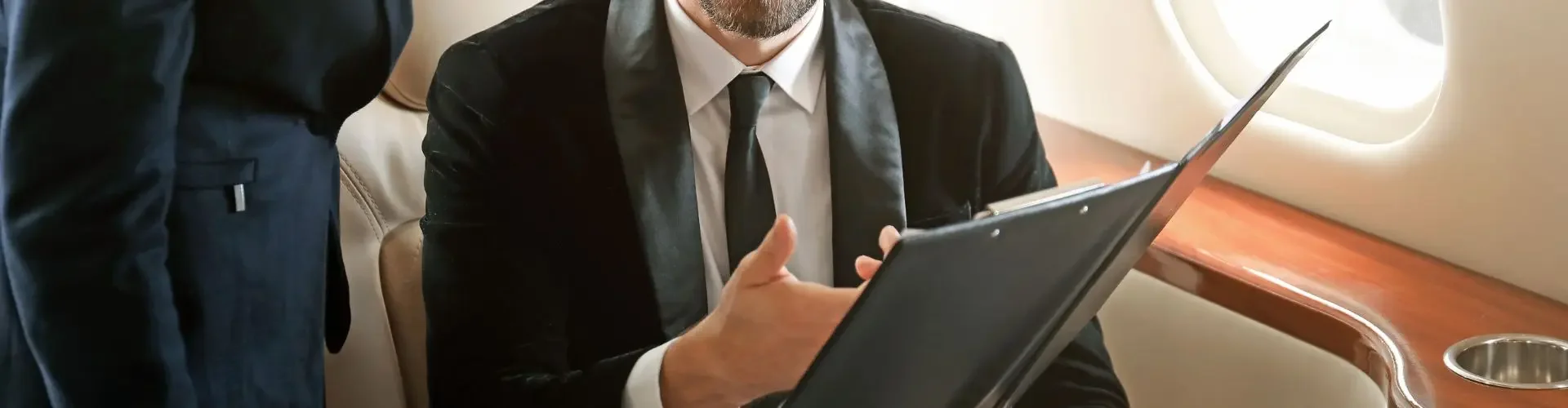 Business executive reviewing documents while flight attendant provides personalized service aboard luxury jet