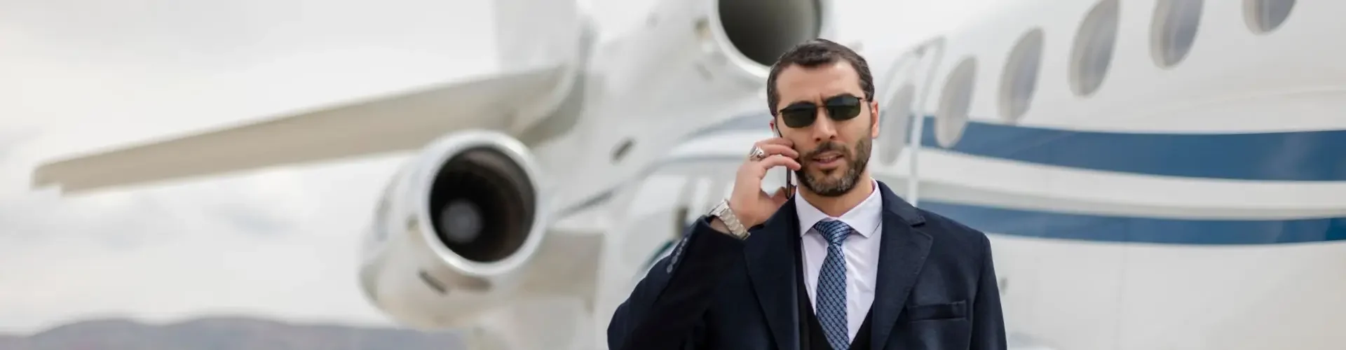 Is a Private Jet Membership Worth It? Business executive in navy suit speaking on phone beside luxury private jet on airport tarmac