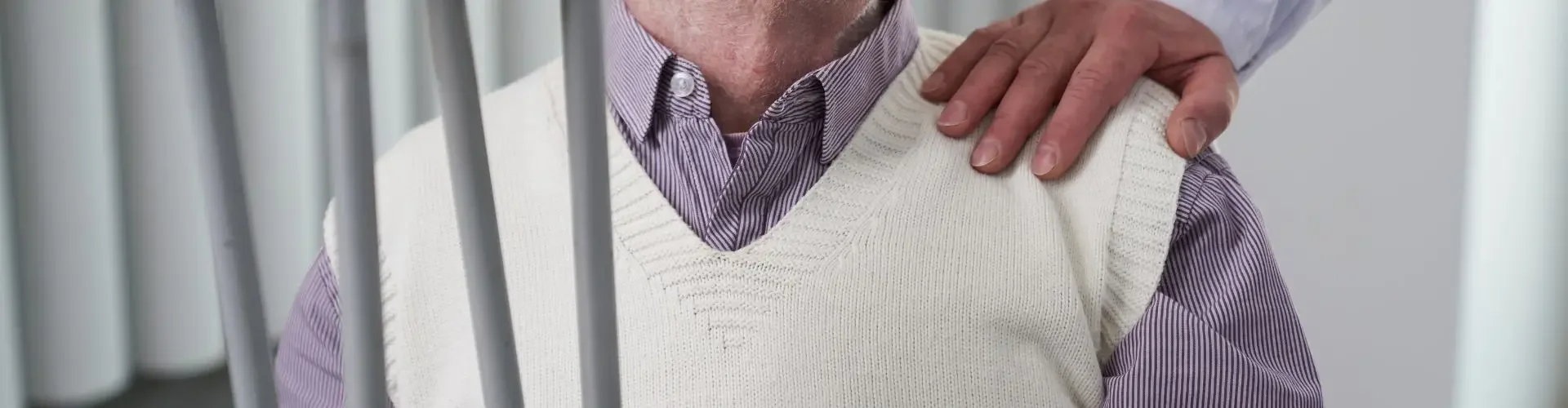 Elderly man with glasses smiling while receiving caring assistance from medical professional in bright clinical setting