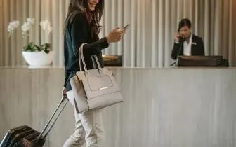 Business traveler with luggage checking phone at luxury hotel reception desk for private jet trip