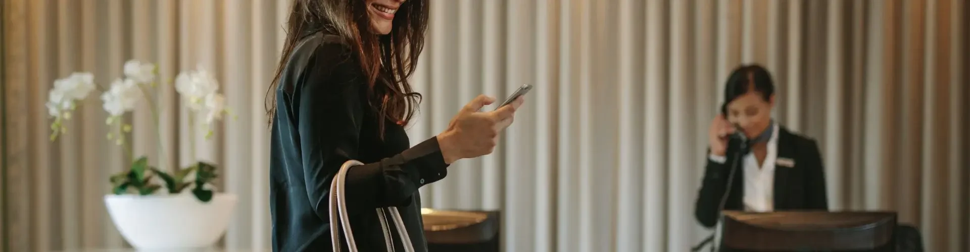 Business traveler with luggage checking phone at luxury hotel reception desk for private jet travel
