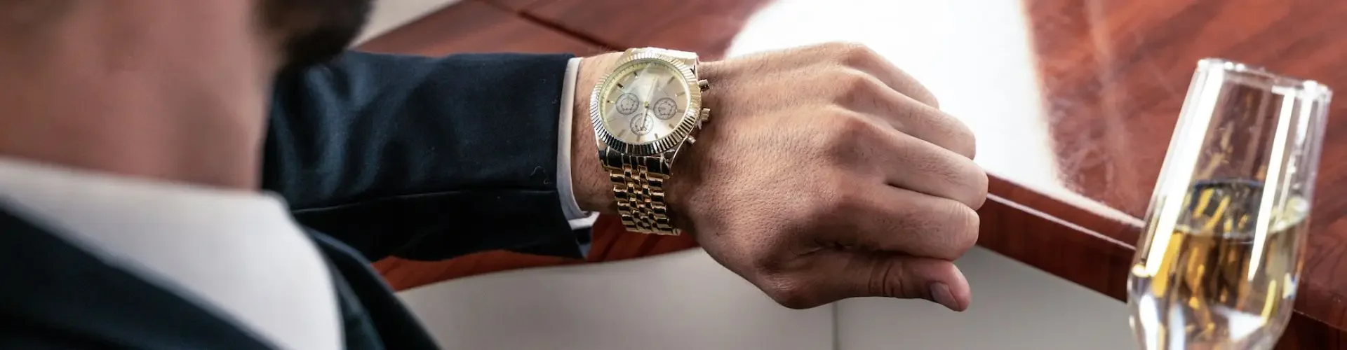 What Is the Least Expensive Way to Fly Privately? Business executive checking luxury watch while holding champagne glass aboard private jet cabin