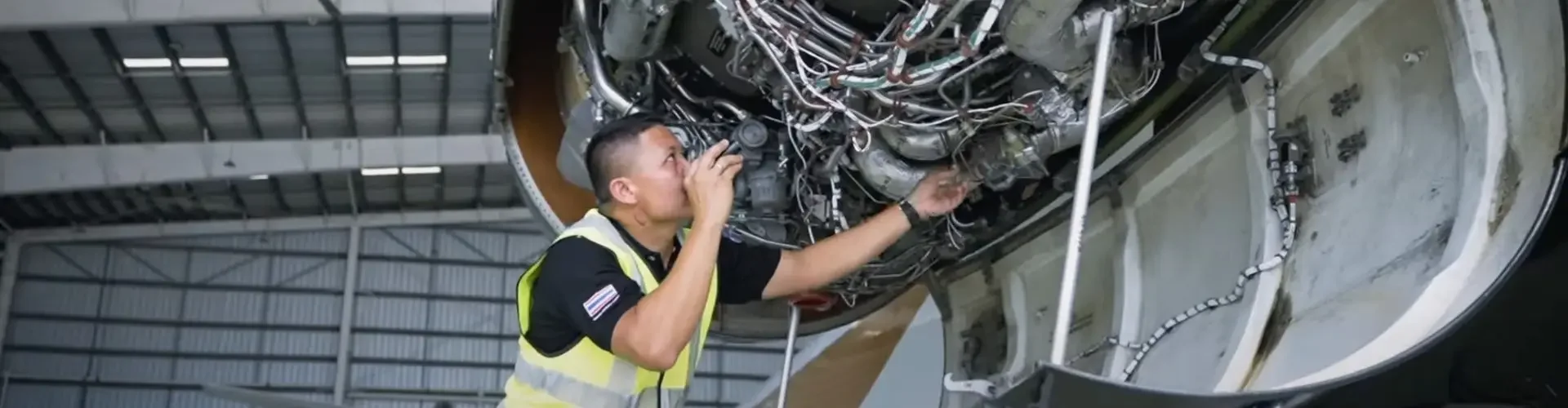 Aircraft maintenance technician inspecting complex wiring systems inside private jet engine compartment