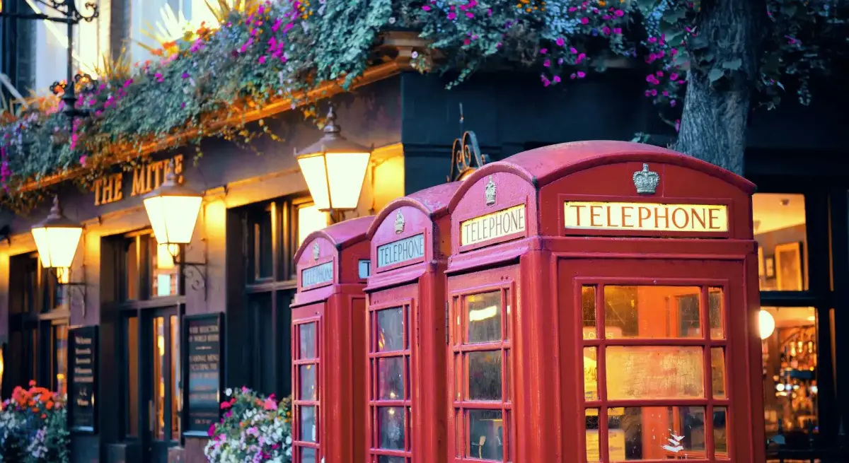 Classic red telephone boxes line a charming London street decorated with festive winter flowers and warm lighting