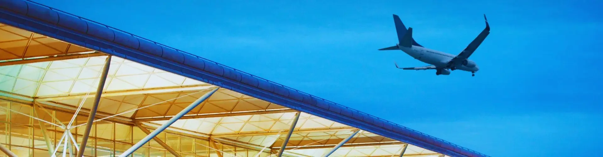 Modern London Stansted Airport terminal with glass architecture and aircraft overhead at dusk