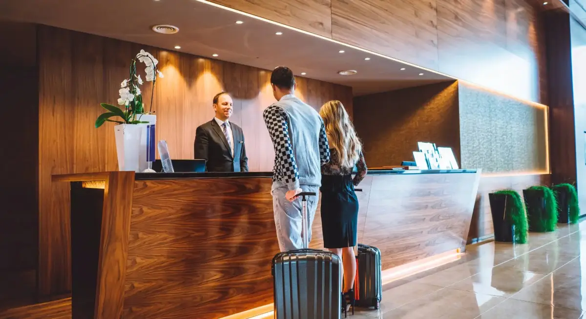 Couple with luggage checking in at luxury hotel reception desk for private jet travel departure