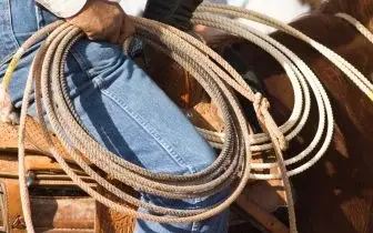 Cowboy holding coiled lasso rope while wearing denim, representing authentic rodeo culture and western travel