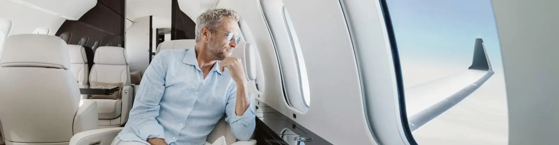 Mature businessman in light blue shirt relaxing in luxury private jet cabin during flight