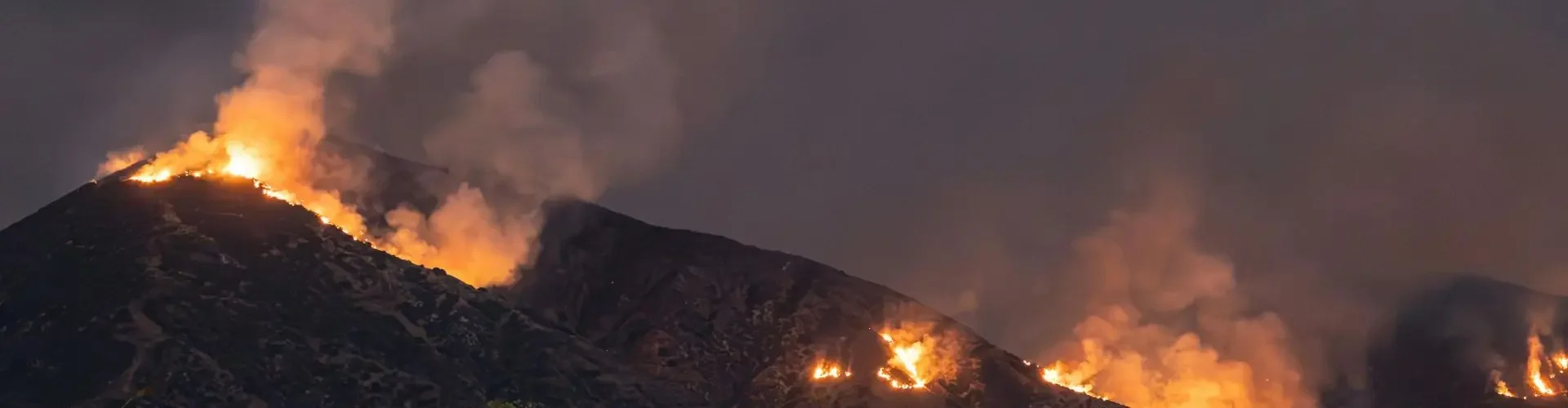 Wildfire flames and smoke engulfing mountainous terrain during climate disaster emergency evacuation scenario
