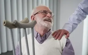 Elderly man with glasses smiling while receiving caring assistance from medical professional in bright clinical setting