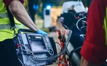 US Bed-to-Bed Transfer Explained Emergency medical technician operating portable defibrillator during critical patient transport procedure