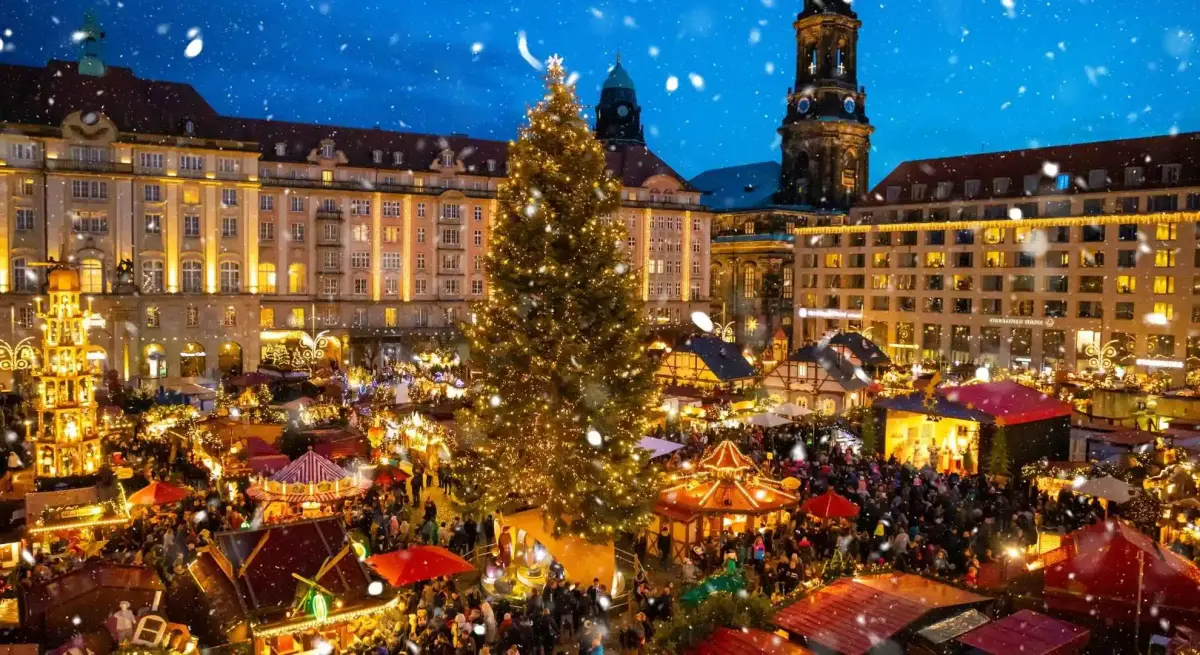 Enchanting Dresden Christmas market with illuminated stalls, towering tree, and baroque architecture under falling snow