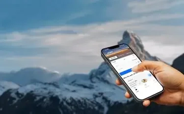 Hand holding smartphone displaying private jet booking app interface against snow-capped mountain backdrop
