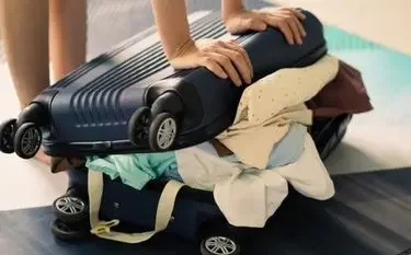 Hands packing luxury clothing into black suitcase for private jet travel with flexible baggage policies