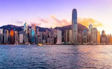 Hong Kong skyline at sunset with gleaming skyscrapers reflecting golden light across Victoria Harbour