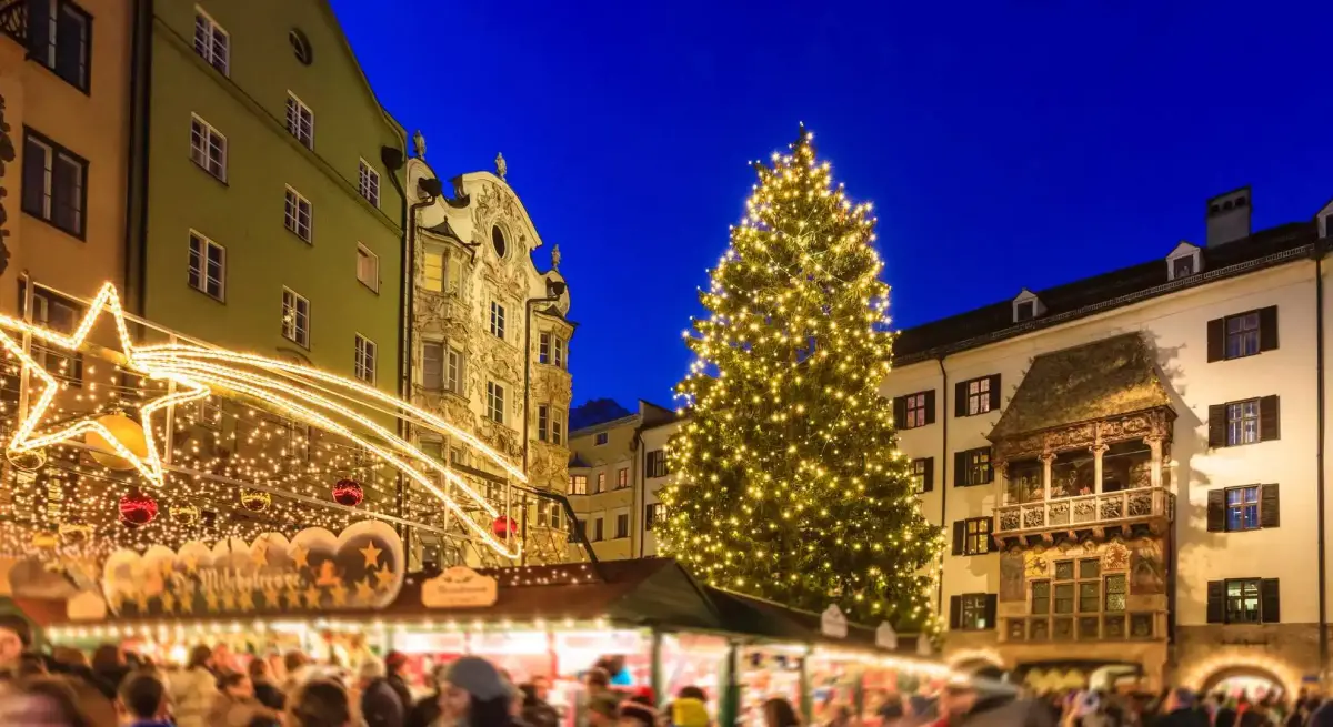 Illuminated Christmas market in historic European town square with towering tree and festive decorations
