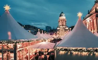 Illuminated Christmas market stalls with white peaked tents beneath historic German cathedral at twilight