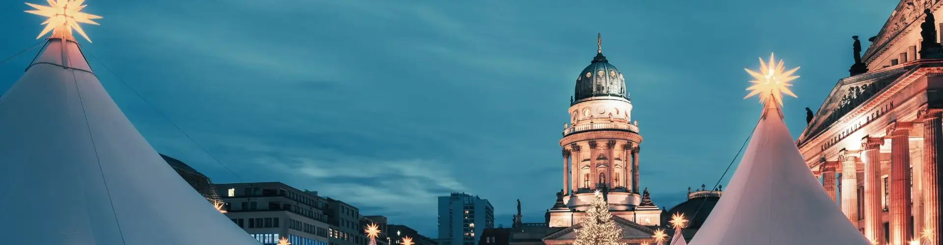 Illuminated Christmas market stalls with white peaked tents beneath historic German cathedral at twilight