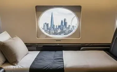 Private Jet Cost in the UK: Route & Aircraft Guide Luxurious private jet cabin bed with city skyline view through oval window during flight over urban landscape