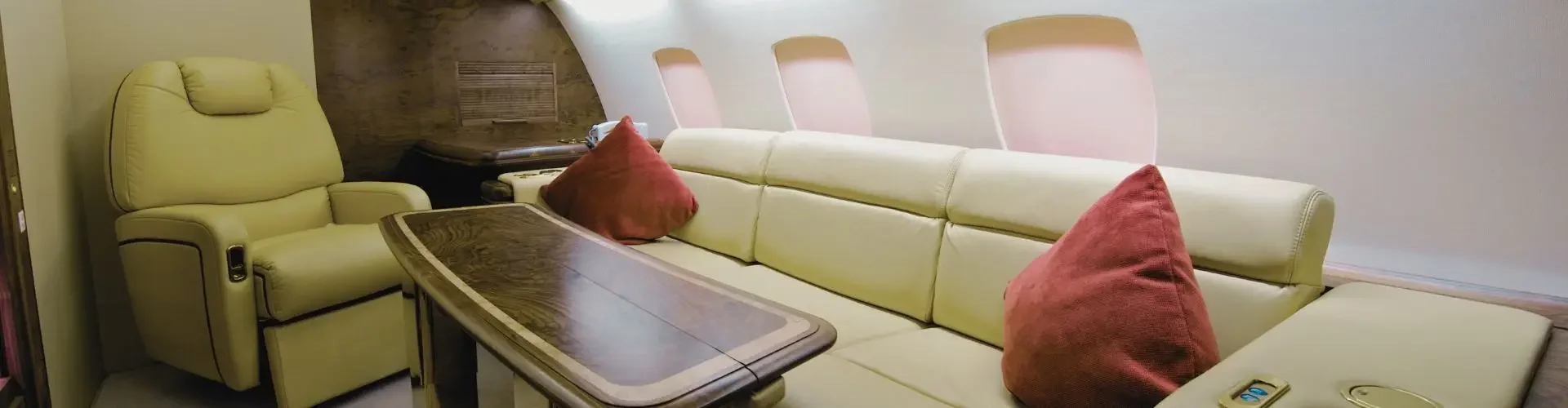Luxurious private jet cabin interior featuring cream leather seating, polished wood table, and panoramic windows