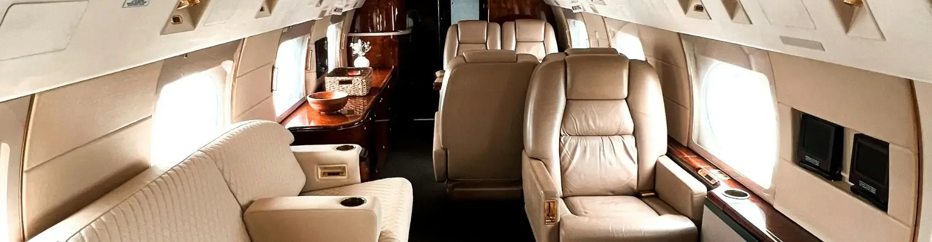Spacious private jet cabin interior featuring cream leather seats and polished wood accents for luxury travel
