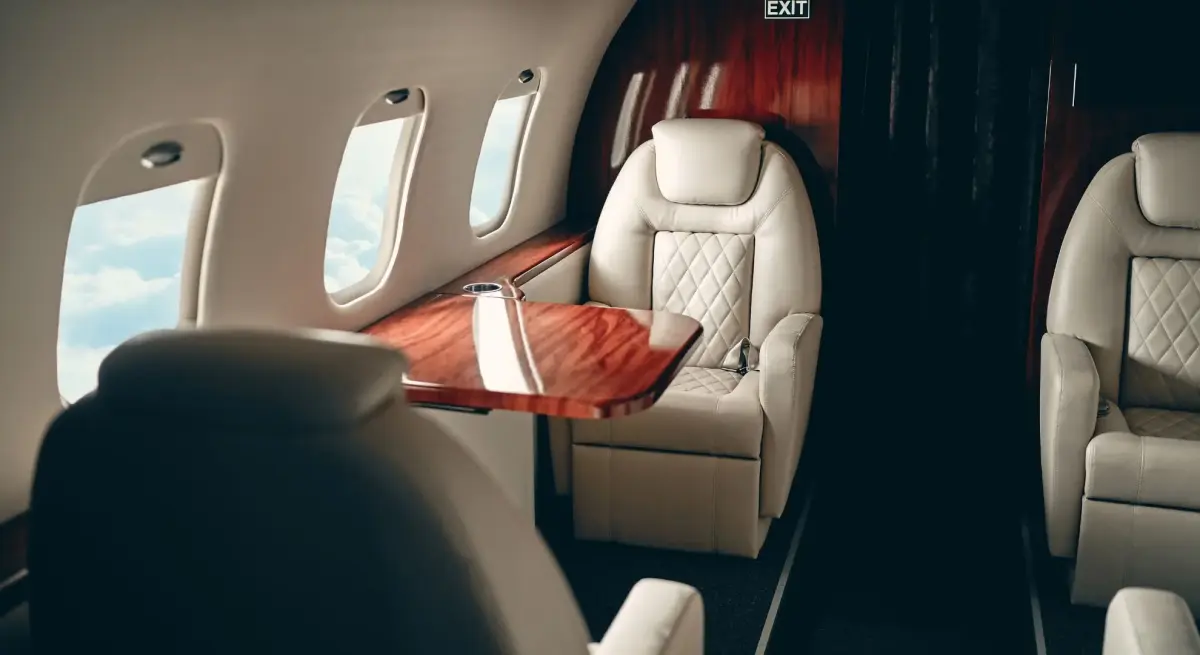 Luxurious private jet cabin interior with quilted leather seats and polished wood table showcasing premium travel comfort