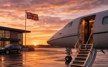 Luxury private jet with boarding stairs on UK tarmac at sunset with British flag and terminal building