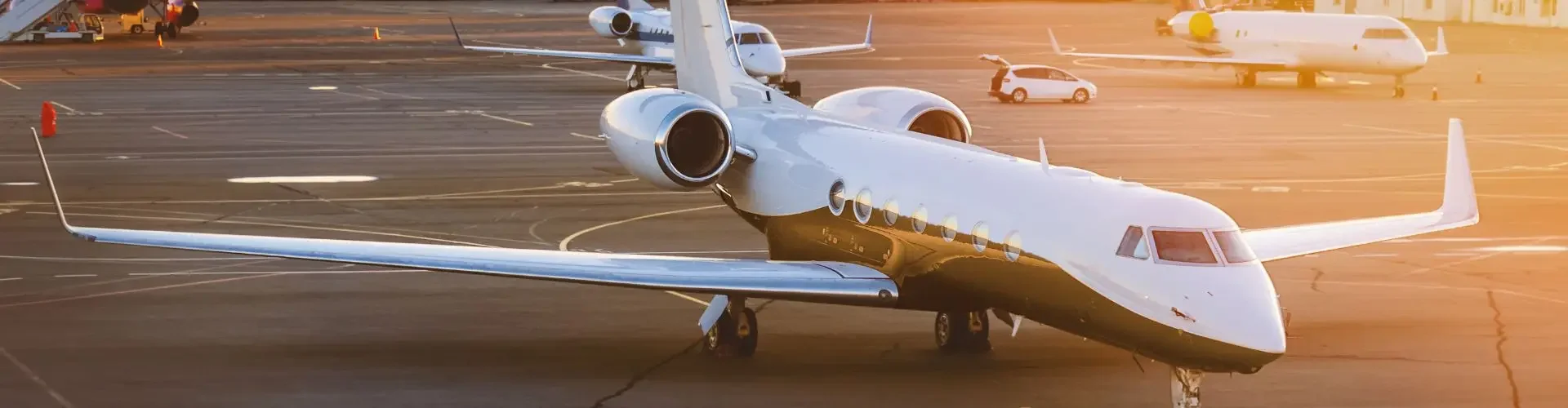 White private jet parked on airport tarmac during golden hour sunset with terminal buildings visible