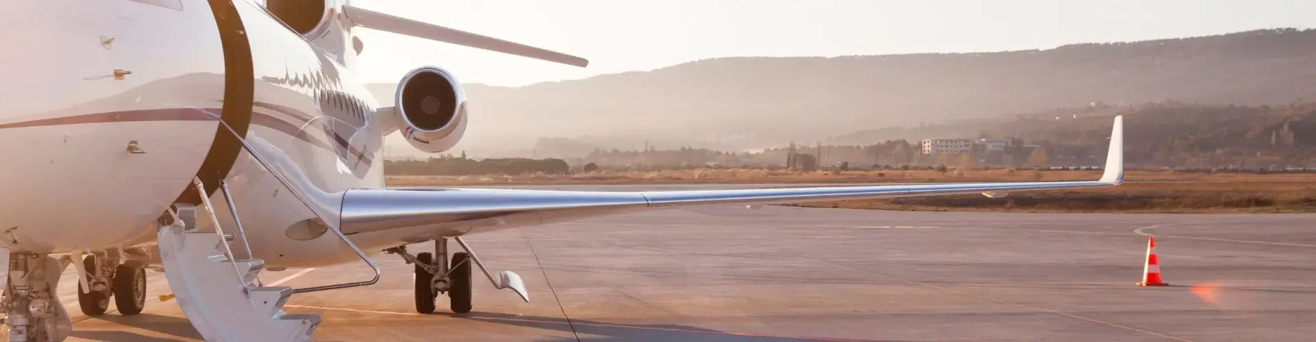 White private jet parked on airport tarmac at sunset with mountains in background for luxury travel